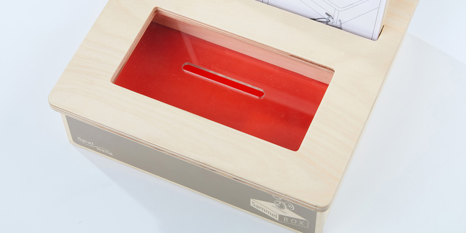 Die SammelBox hat eine transparente Scheibe auf der Oberseite mit einem Schlitz für Münzen und Scheine, die den Blick auf die Spenden ermöglicht.